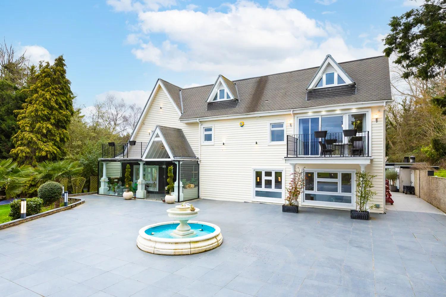 Bluebell House by day — white weatherboard facade, stone fountain courtyard, blue sky