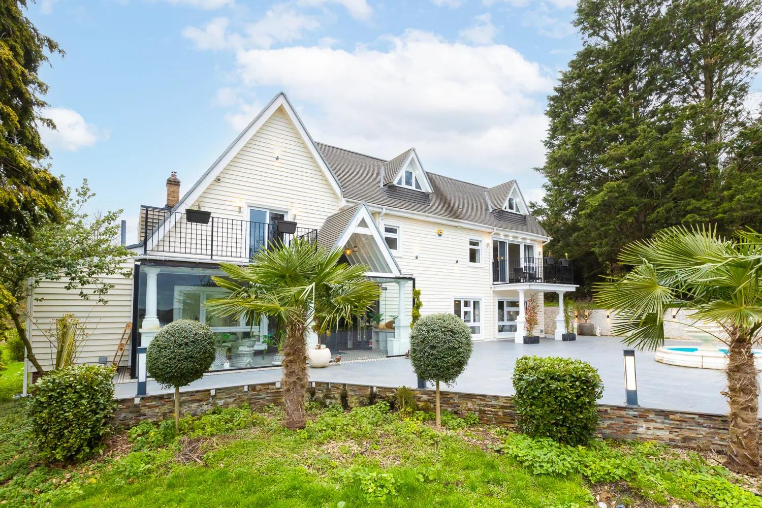 Bluebell House from the garden — white weatherboard, fan palms, glass extension, balcony